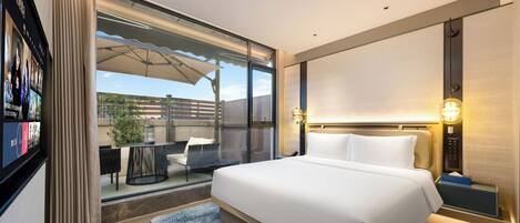 Una habitación de hotel moderna con una cama grande, televisión, escritorio con silla y vistas al exterior.