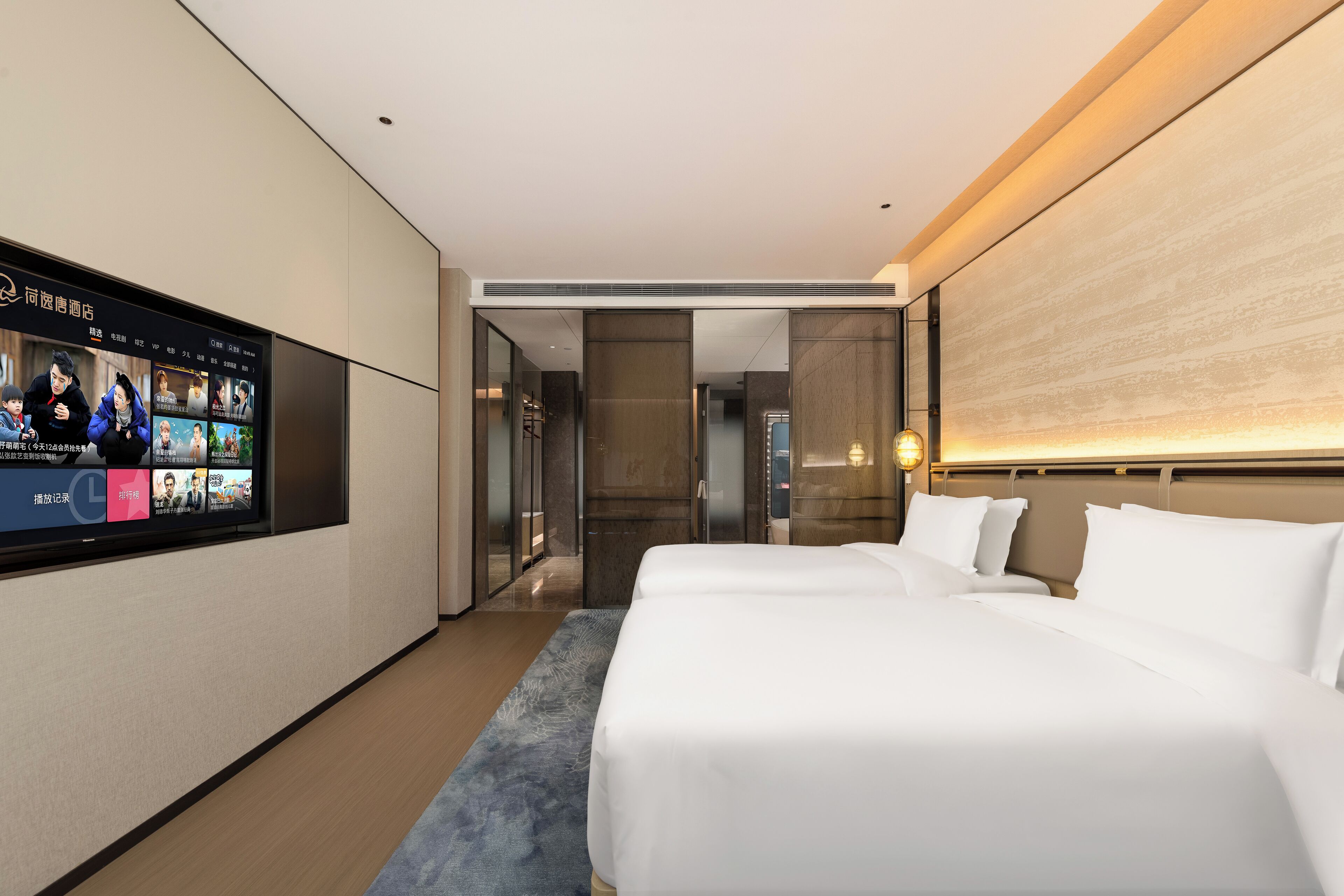 Una habitación de hotel moderna con una cama grande, un televisor mostrando una película y un pasillo que conduce a un baño.