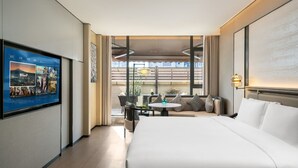 Une chambre d’hôtel avec un grand lit, un téléviseur fixé au mur, un balcon avec une table et des chaises, et une vue sur la ville.