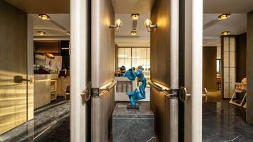 A modern hotel lobby with marble floors, a central staircase, and a decorative blue sculpture.