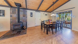 A dining area with a wooden table and chairs, a stone fireplace, and a view through glass doors to an outdoor patio.