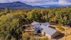 A large, single-story building with a metal roof, surrounded by dense trees and a mountainous backdrop.