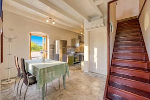 A dining area with a table and chairs, a kitchen in the background, and a wooden staircase.
