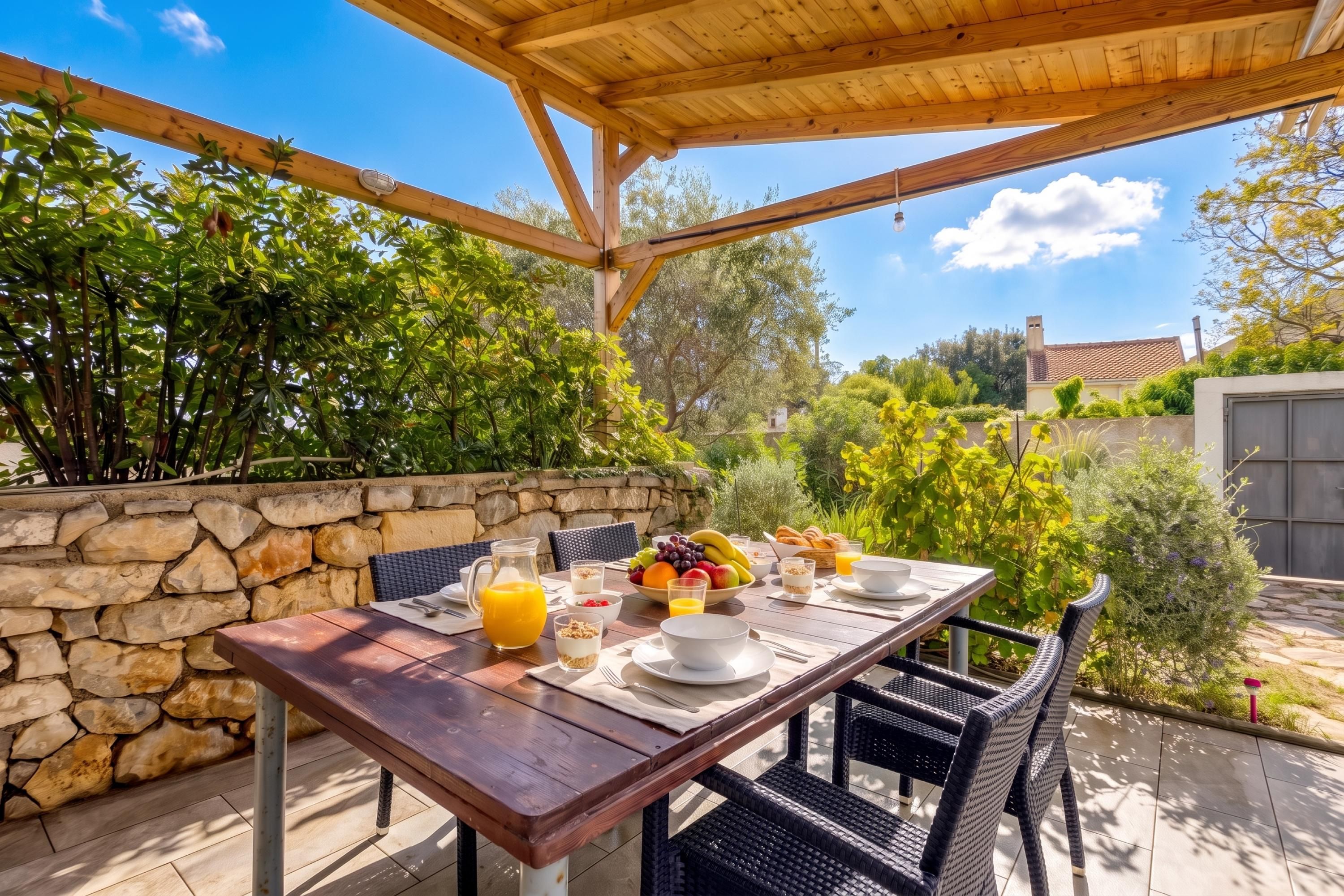 Un área de comedor al aire libre con pared de piedra, mesa y sillas de madera.