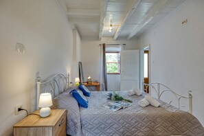 Un dormitorio con cama, mesita de noche, lámpara y ventana con cortinas.
