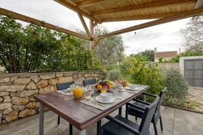 Un comedor al aire libre con pared de piedra, pérgola de madera y una mesa servida con desayuno.