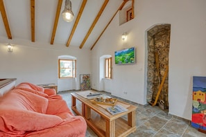 Una habitación acogedora con techo de madera, un sofá, una mesa con bandeja, un cuadro y una pared de piedra.