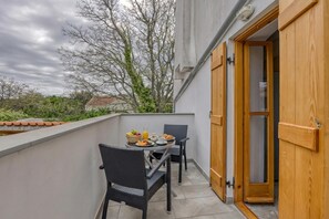 Ein Balkon mit Frühstückstisch, Korbstühlen und einer Holztür.