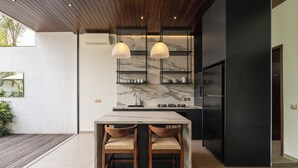 A modern kitchen with a marble countertop, two wooden bar stools, pendant lights, and black cabinetry. - Rocca Bella Loft 2 by Alfred in Bali (Canggu)