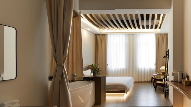 A modern hotel room with a large bed, a sitting area with a table and chairs, a bathtub, and a large mirror. - Zen Den Design (Shantou)