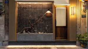 A modern hotel entrance with a textured wall, a wooden door, and a small potted plant. - Zen Den Design (Shantou)