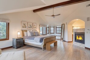 Cozy retreat with a large bed, fireplace, and high ceiling with exposed beams.