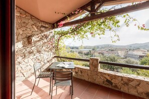 Ein Balkon mit Steinmauern, einem Tisch mit Stühlen und Blick auf eine Stadt und Hügel.