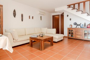 Una sala de estar con un sofá, una mesa de centro de madera, un aparador con objetos decorativos y una escalera.