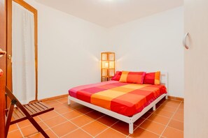 A bedroom with a bed, a chair, a nightstand, and a wall-mounted lamp.