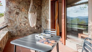Een balkon met een stenen muur, een hangstoel, een tafel met een boek en uitzicht op het landschap.