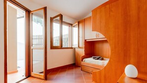 Une chambre avec une porte-fenêtre coulissante, un lit, un bureau et un petit placard.