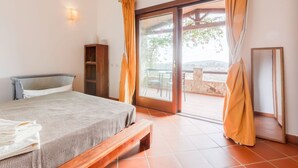 Een slaapkamer met een bed, een houten bankje, een kledingkast en een schuifdeur naar een buitenruimte.