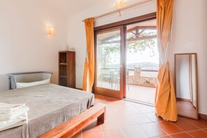 Ein Schlafzimmer mit einem Bett, einer hölzernen Bank, einem Kleiderschrank und einer Glastür, die zu einem Außenbereich führt.