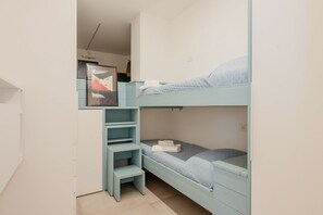 Un lit superposé avec un bureau et des étagères intégrés, une affiche accrochée au mur et une petite fenêtre.