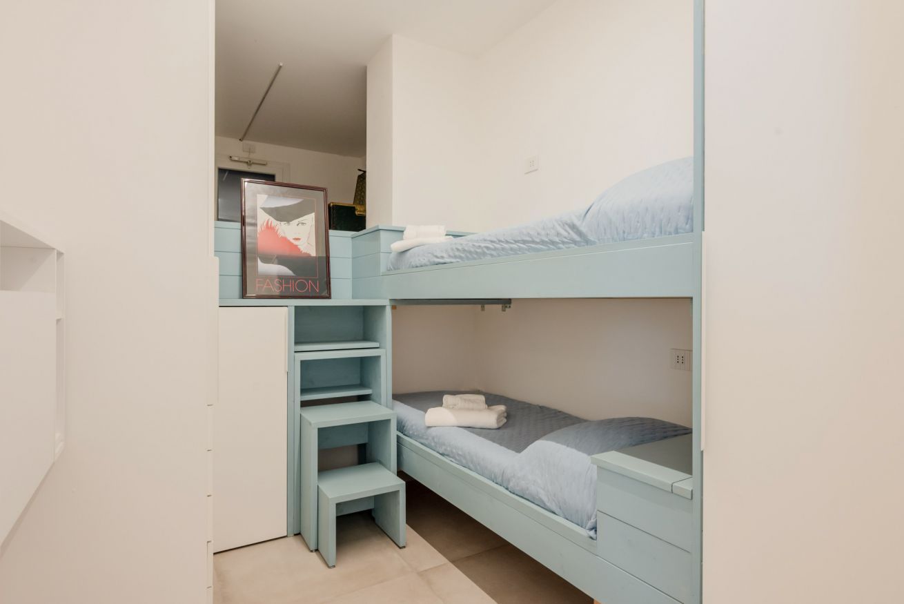 A bunk bed with a built-in desk and shelving, a poster on the wall, and a small window.