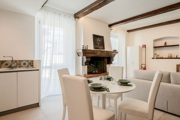 Un comedor con una mesa redonda, sillas blancas, una chimenea y una cocina al fondo.