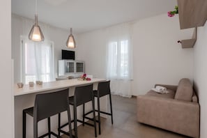 A modern kitchen with a dining area, a sofa, and a TV. - GuestHost - Mare Monti Apartment 4 (Dogana)