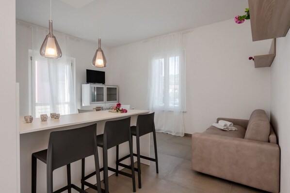 A modern kitchen with a dining area, a sofa, and a TV.