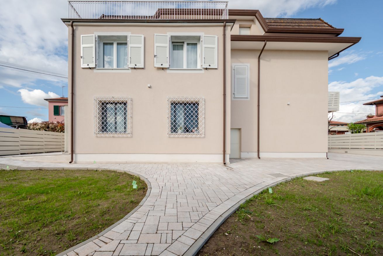 A two-story building with a paved walkway, two windows with shutters, and a small balcony.