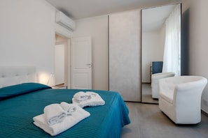 A modern hotel room with a bed, a chair, a mirror, and a door. - GuestHost - Mare Monti Apartment 4 (Dogana)