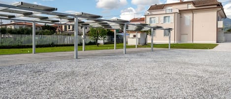 A building with a modern design, a covered outdoor area with a gravel floor, and a fence in the background.
