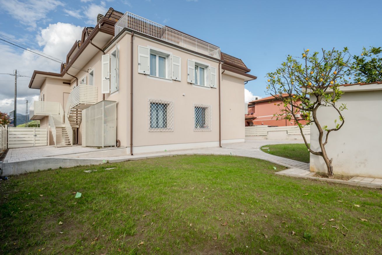 Un immeuble résidentiel de deux étages doté d’un balcon, d’un petit jardin et d’un arbre.