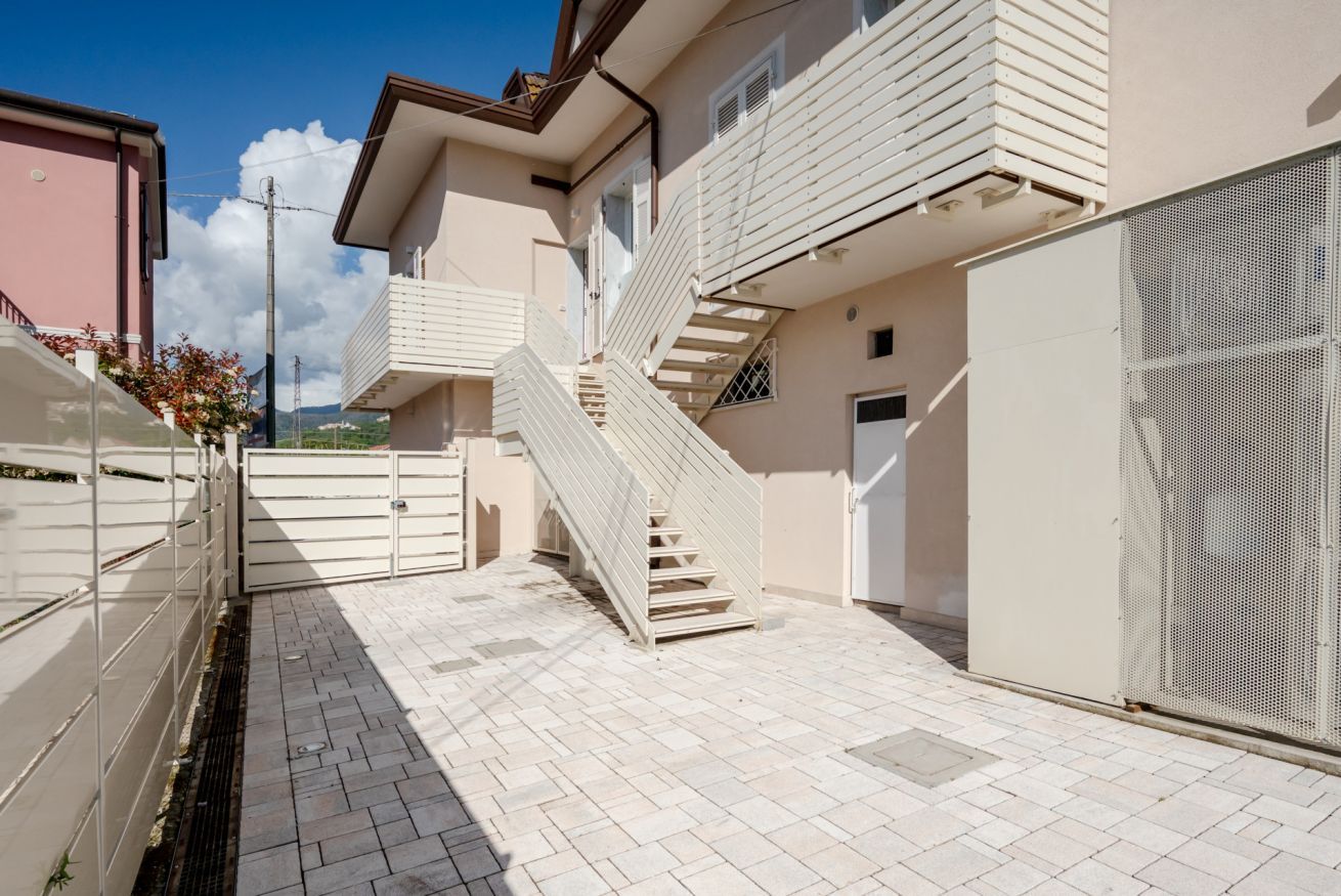 A residential building with a staircase leading to an upper floor, a gated entrance, and a view of the surrounding area.