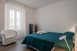 A bedroom with a bed, a chair, a bedside table, and a window with curtains.