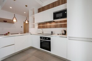 A modern kitchen with white cabinetry, a built-in oven, a microwave, and pendant lighting.