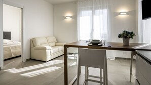 A modern, well-lit room with a dining table, a sofa, and a TV mounted on the wall.