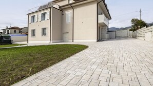 A modern two-story house with a paved driveway, a small lawn, and a mountain backdrop.