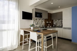A modern kitchen with a dining area, a flat-screen TV mounted on the wall, and a window with sheer curtains. - GuestHost - Mare Monti Apartment 5 (Dogana)