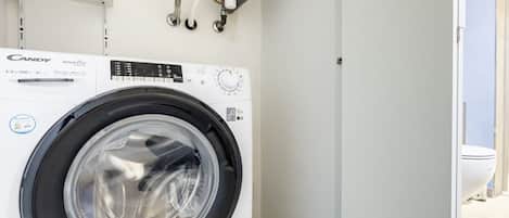 A Candy SmartPro washing machine in a laundry room with a white wall and a visible toilet in the background.