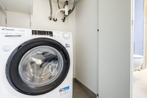 A Candy SmartPro washing machine in a laundry room with a white wall and a visible toilet in the background. - GuestHost - Mare Monti Apartment 5 (Dogana)