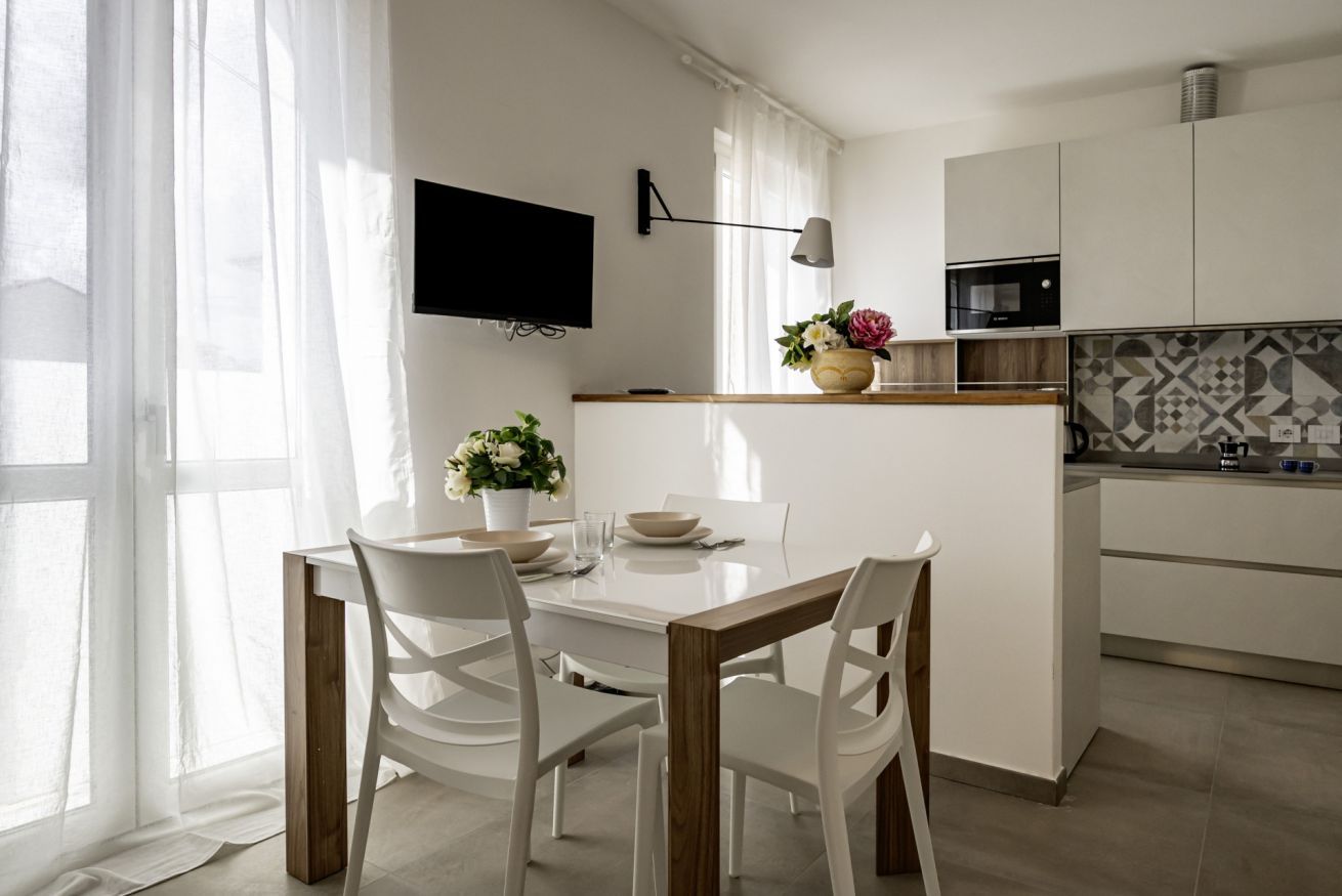 Une cuisine moderne avec un coin repas, un téléviseur à écran plat et un petit îlot central agrémenté d’un vase de fleurs.