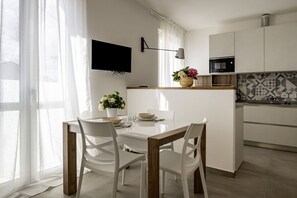 A modern kitchen with a dining area, a flat-screen TV, and a small island with a vase of flowers.