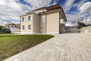 A modern two-story building with a paved driveway and a small grassy area. - GuestHost - Mare Monti Apartment 6 (Dogana)