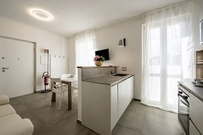 A modern kitchen with a central island, a dining area with a white table and chairs, a sofa, and a TV mounted on the wall.