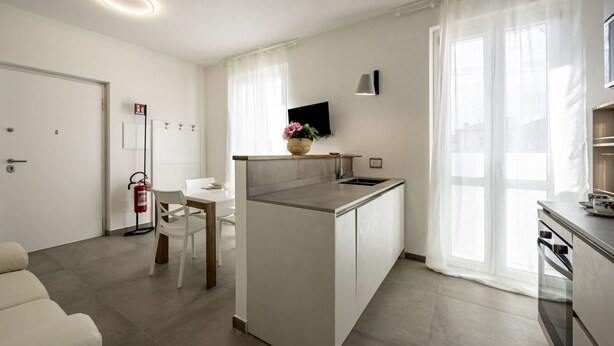 Ett modernt kök med en central köksö, en matplats med ett vitt bord och stolar, en soffa och en tv som är monterad på väggen.