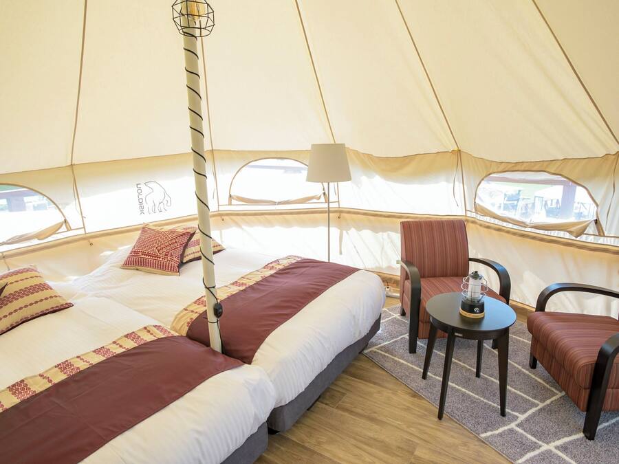 A tented accommodation with a bed, two chairs, a table, and a lamp.