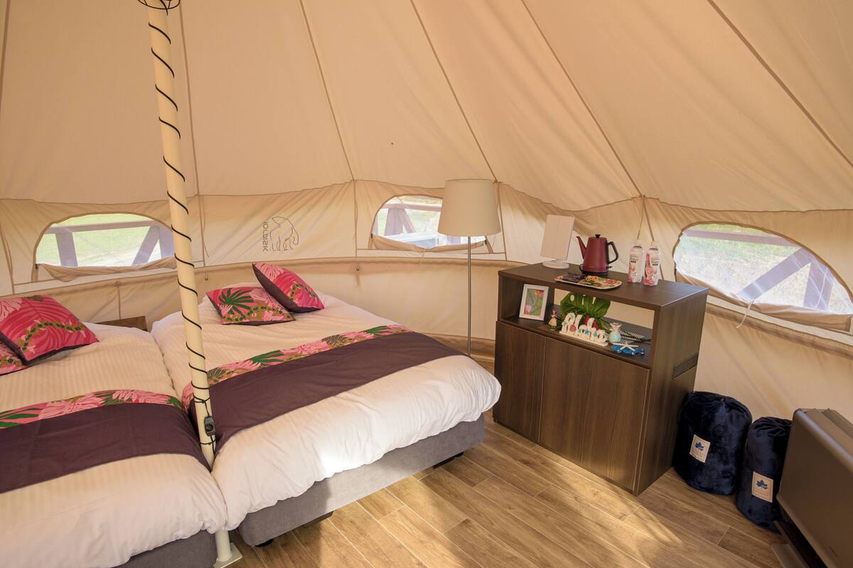 Een tent met twee bedden, een nachtkastje, een lamp en een raam.