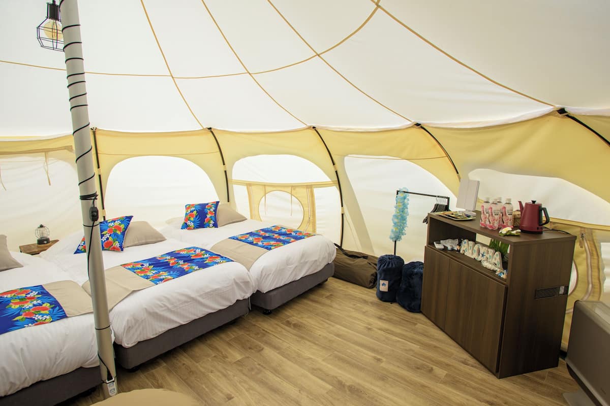 A tent with two beds, a wooden cabinet, and a lamp.