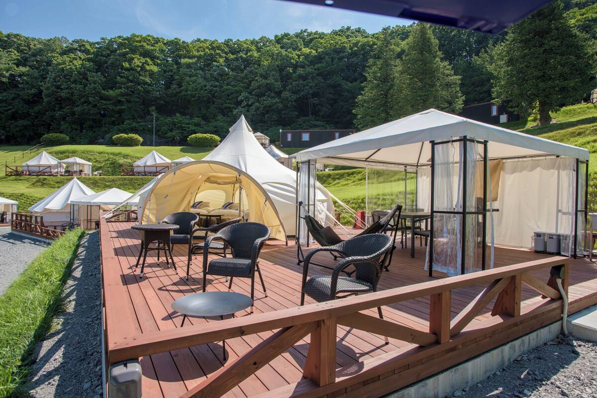 Een houten terras met buitenmeubelen en een grote tentconstructie.