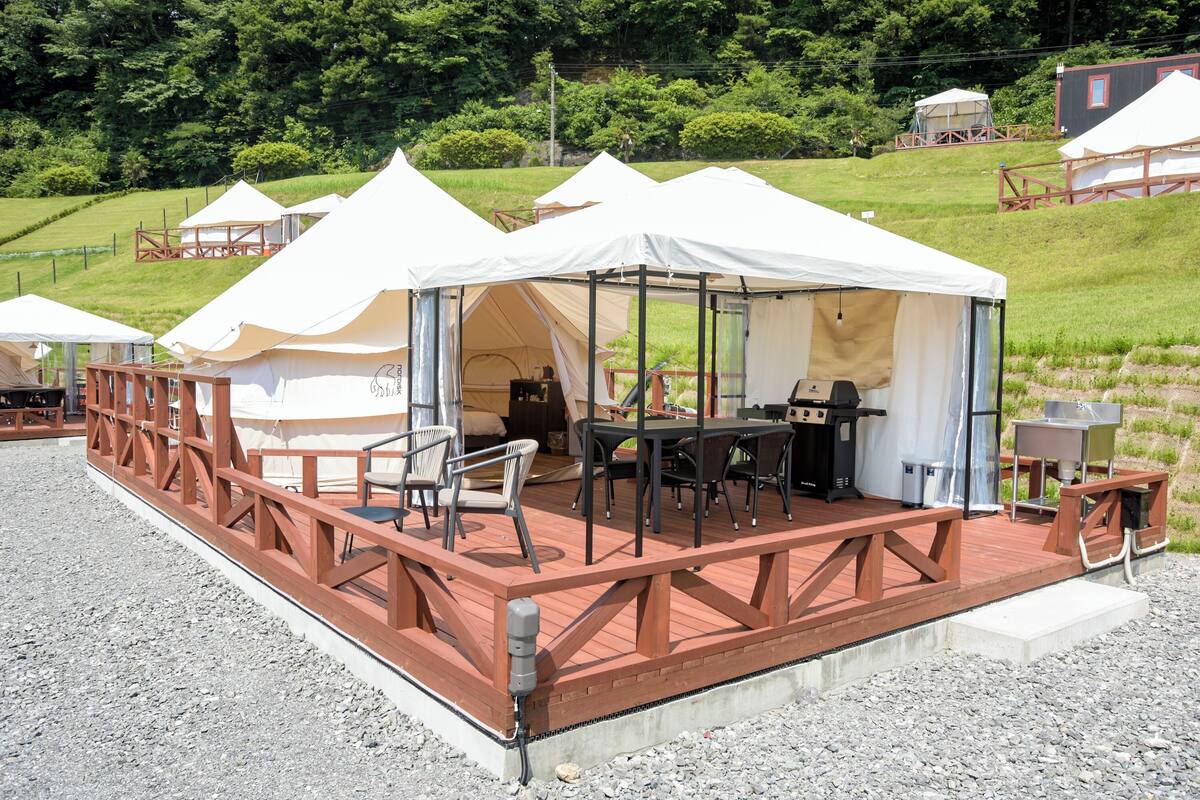 Een reeks tenten met houten dekken en tafels, omgeven door glooiende heuvels.